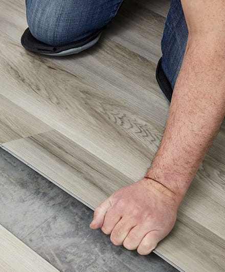 Professional installing luxury vinyl plank flooring in a residential bedroom