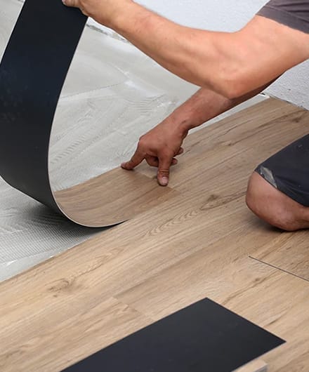 Professional installing luxury vinyl plank flooring in a residential bedroom